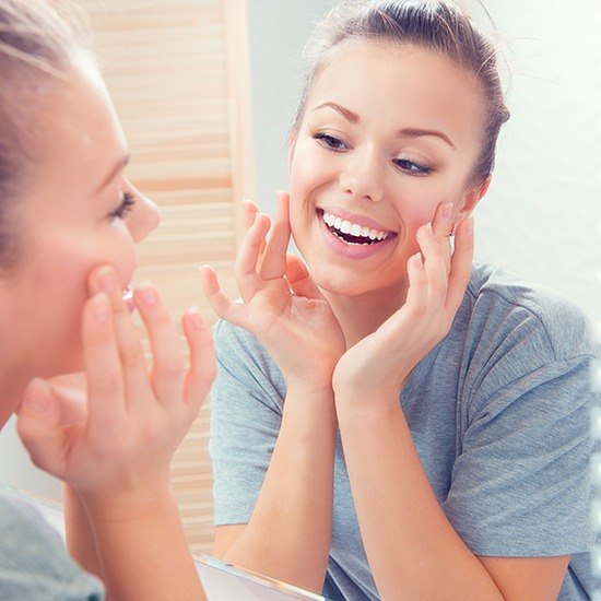 Woman smiling at herself in mirror after botox and juvederm treatment