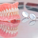 A pair of dentures sitting next to dental mirrors on a glass surface