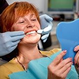 A senior woman looking at her new dentures with a hand mirror