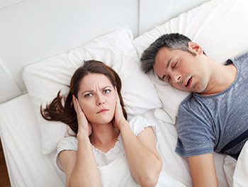 Woman covering ears, annoyed by the snoring of her husband