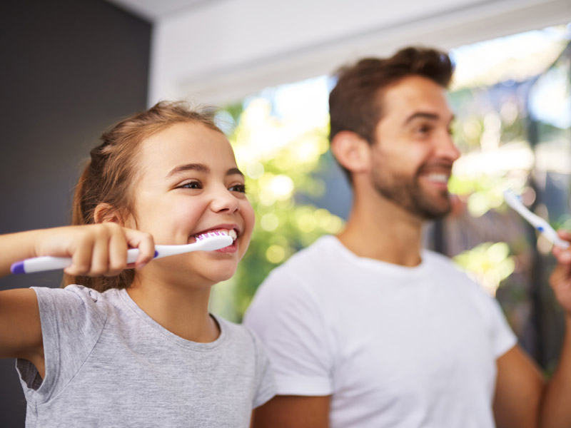 father and daughter brushing their teeth side by side